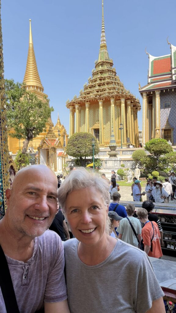 A picture of a couple visiting the Bangkok Grand Palace, specifically in front of a couple grand and opulent smaller temples