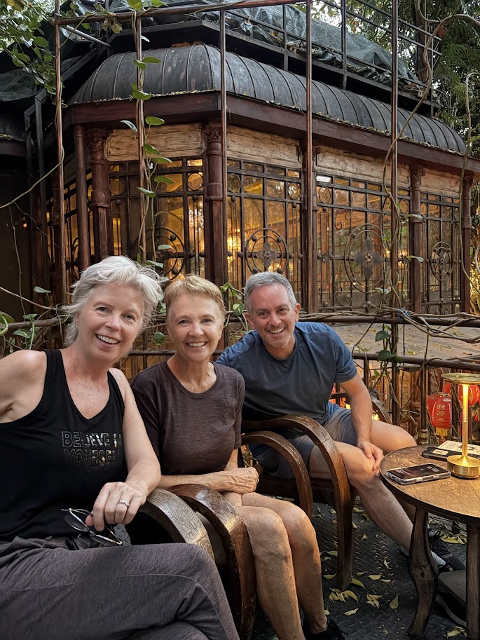 Picture of three adults sitting in Chiang Mai sitting a restaurant that is also an gallery that shows many ancient stone figurines and carvings.