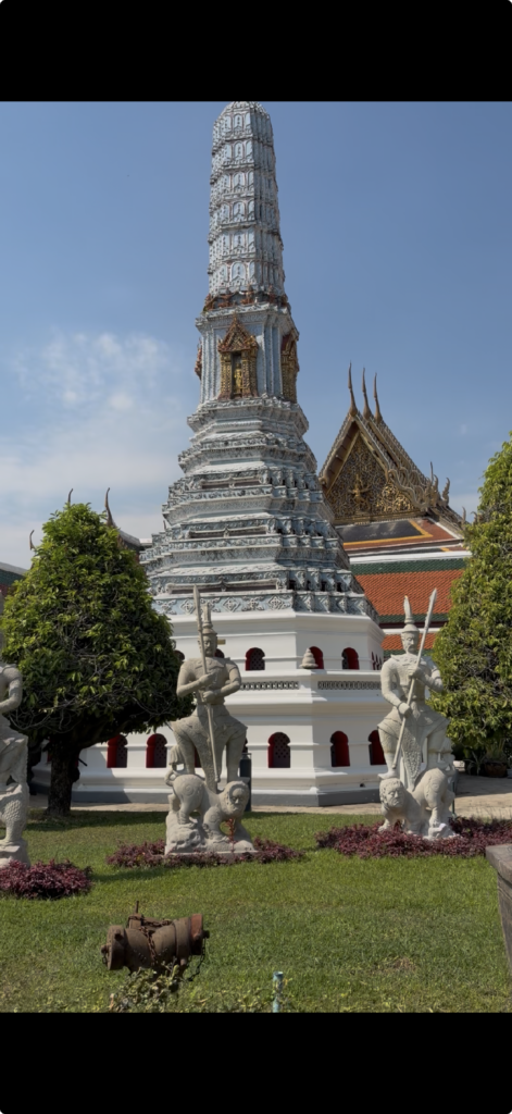 An image of small temple in Bangkok.  It has two guardian type figurines in front of it. 